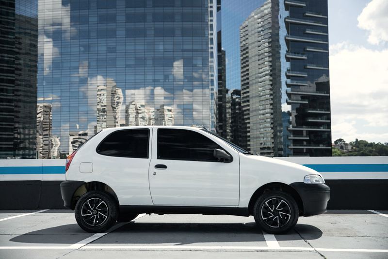 Fiat Palio branco estacionado no alto de um prédio, com edifícios espelhados ao fundo