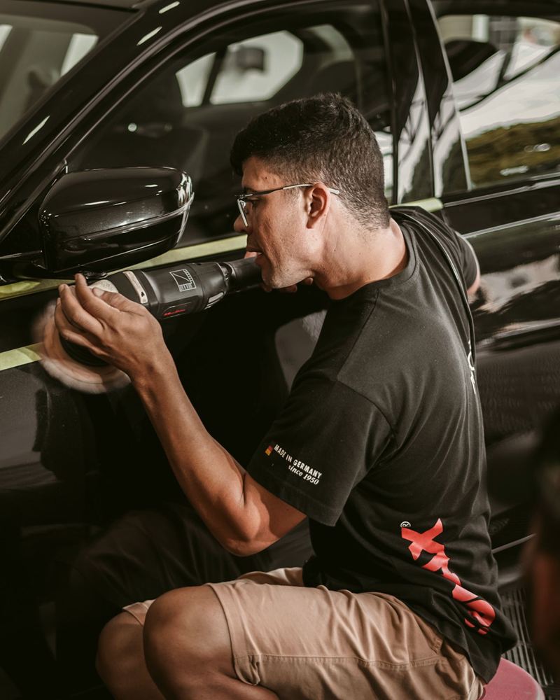 Funcionário polindo com a politriz a lateral de um carro preto, com fita protegendo os frisos
